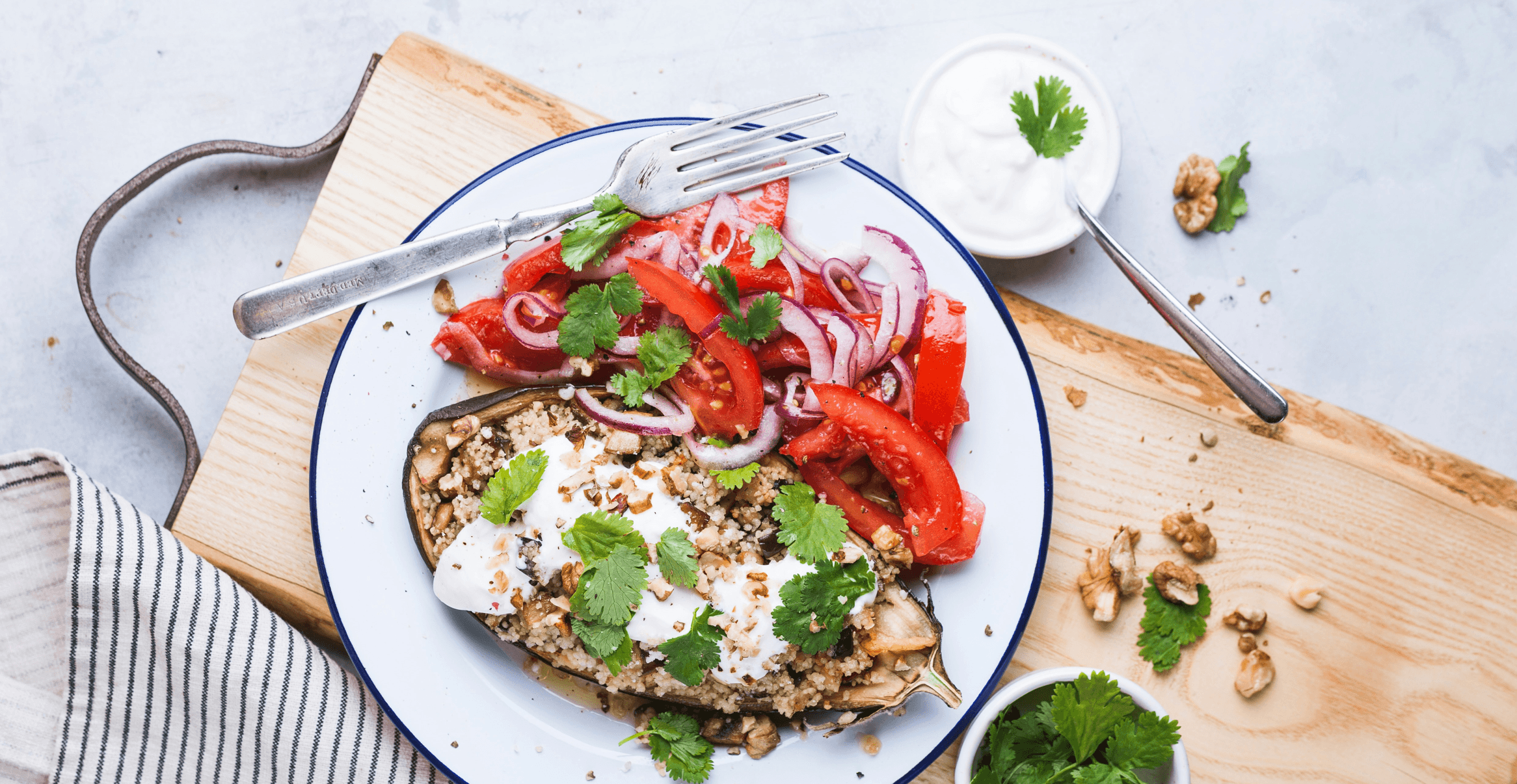 An overhead photo of grilled eggplant with salad, a fork on the plate, and a spare spoon to the side